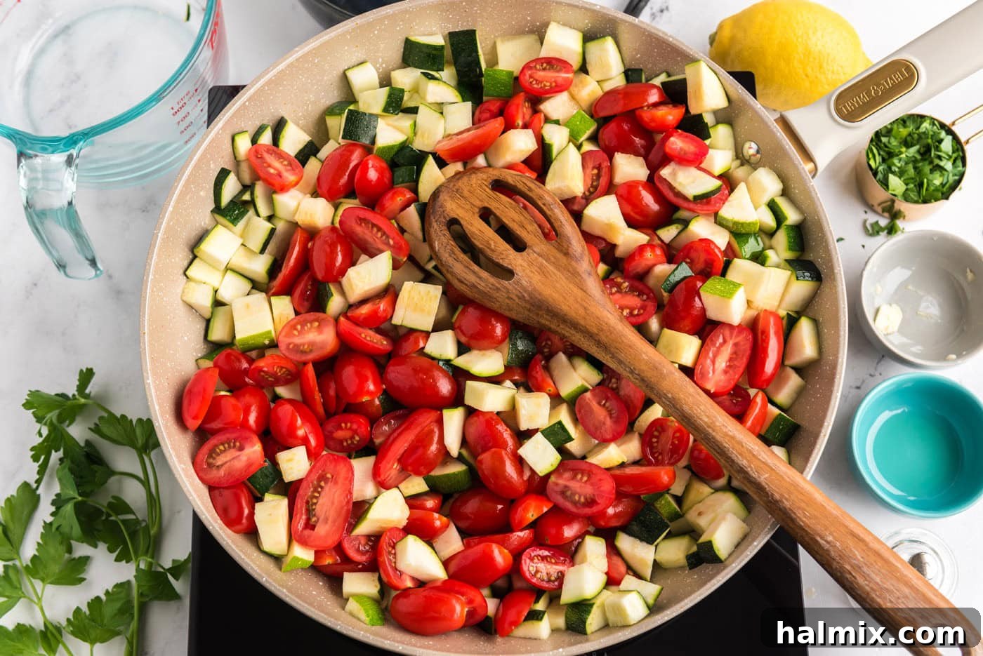 zucchini and grape tomatoes in a skillet with a wooden spoon