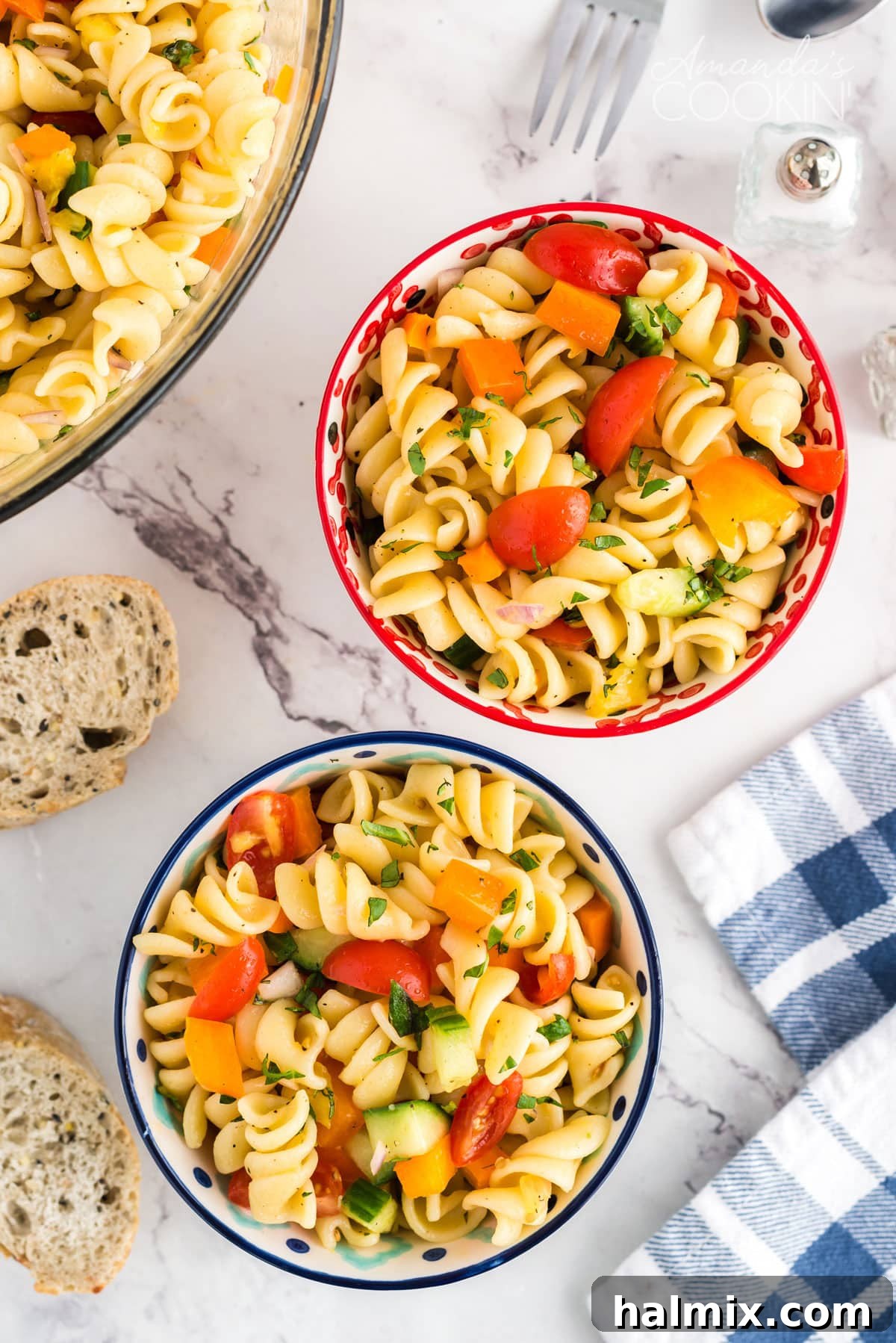 Two bowls of vibrant summer pasta salad on a wooden table with a blue and white tea towel