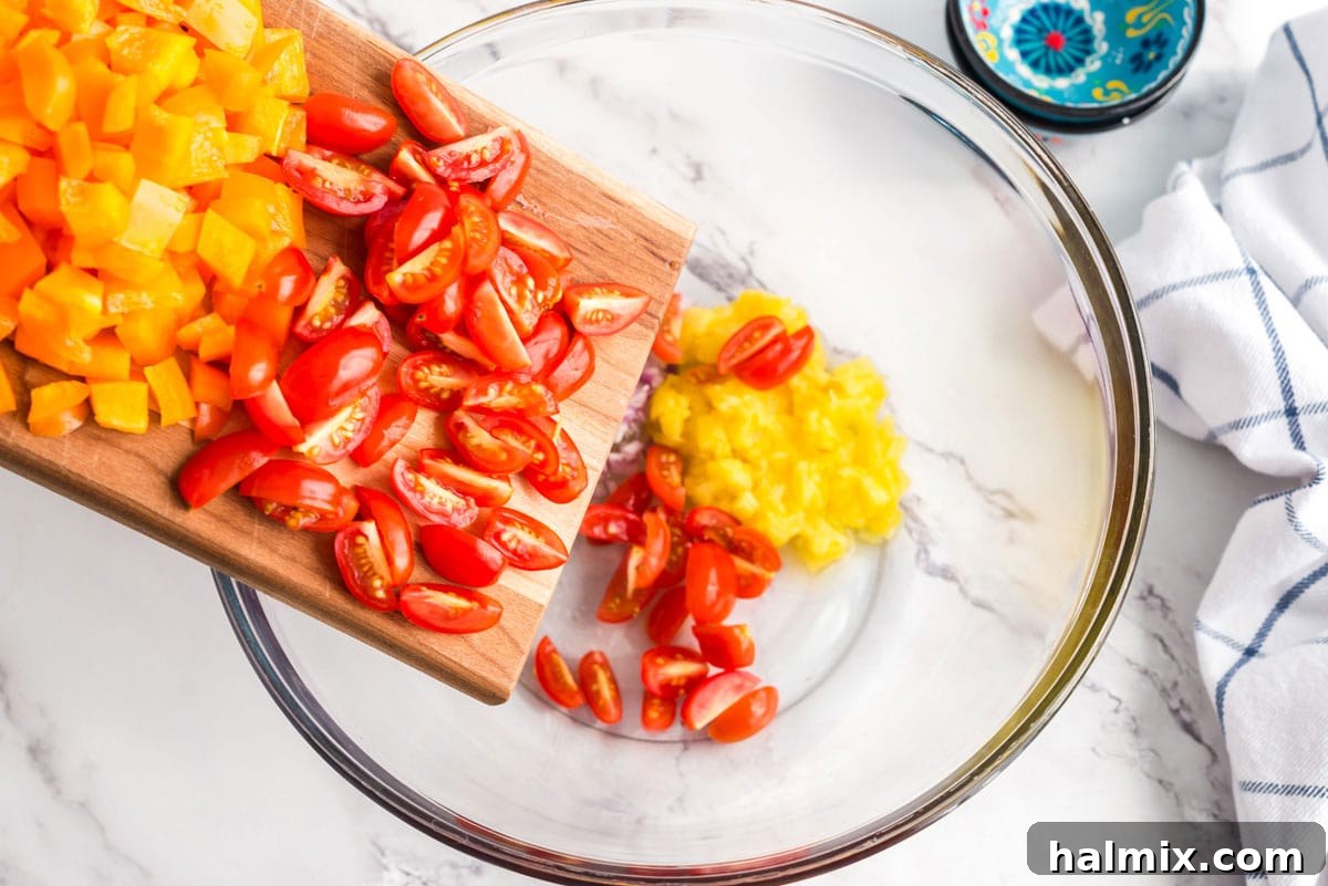 Adding sliced cherry tomatoes to a large bowl of pasta and other chopped vegetables