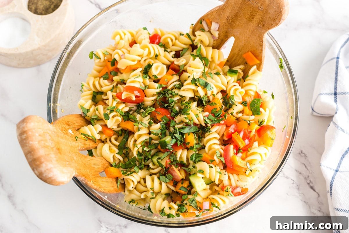 Fresh chopped basil being sprinkled over the colorful summer pasta salad in a bowl