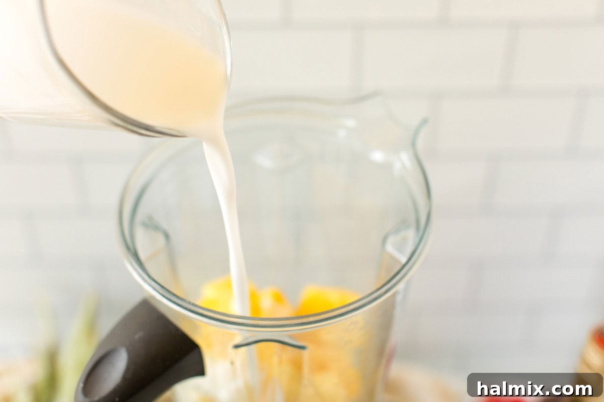 Pouring creamy coconut milk into a high-speed blender, already containing chunks of frozen pineapple, a crucial step for achieving the perfect slush consistency.