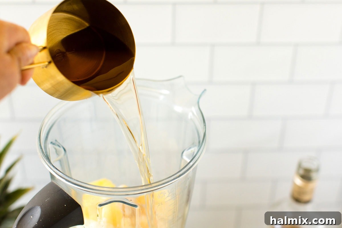 Adding a measured amount of amber-hued rum directly into the blender with the pineapple and coconut milk, combining the core ingredients for the tropical slush.
