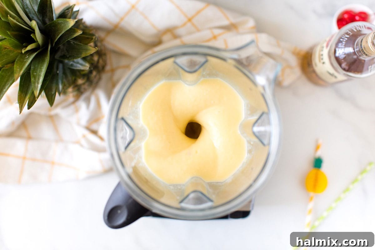 The pineapple rum slush mixture swirling smoothly in a blender, perfectly pureed to a thick, consistent texture, ready for serving.