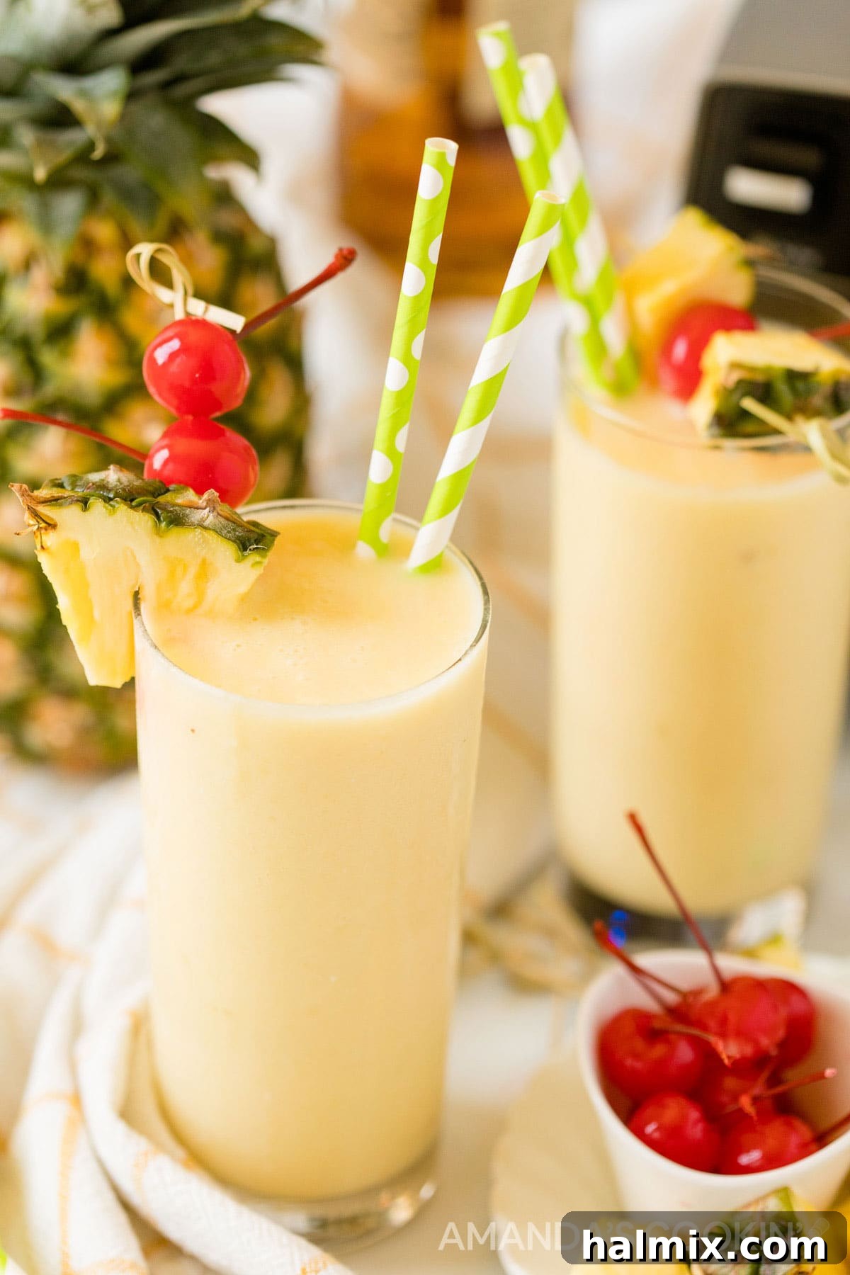 Two enticing glasses of pineapple rum slush, perfectly garnished and ready to drink, with a blender subtly blurred in the background, signaling ease of preparation.
