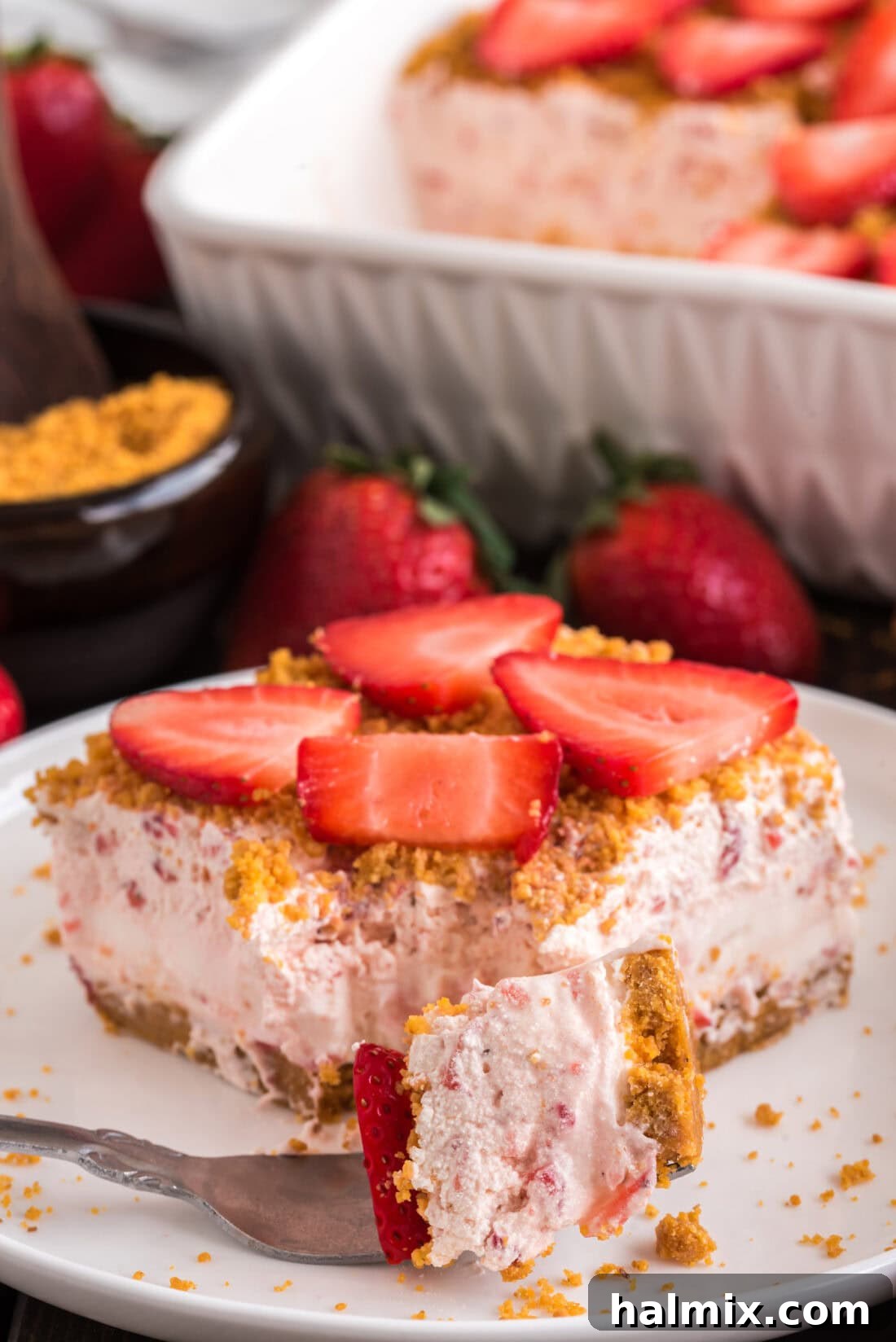 Strawberry Dream Dessert on a fork resting in front of a slice of Strawberry Dream Dessert