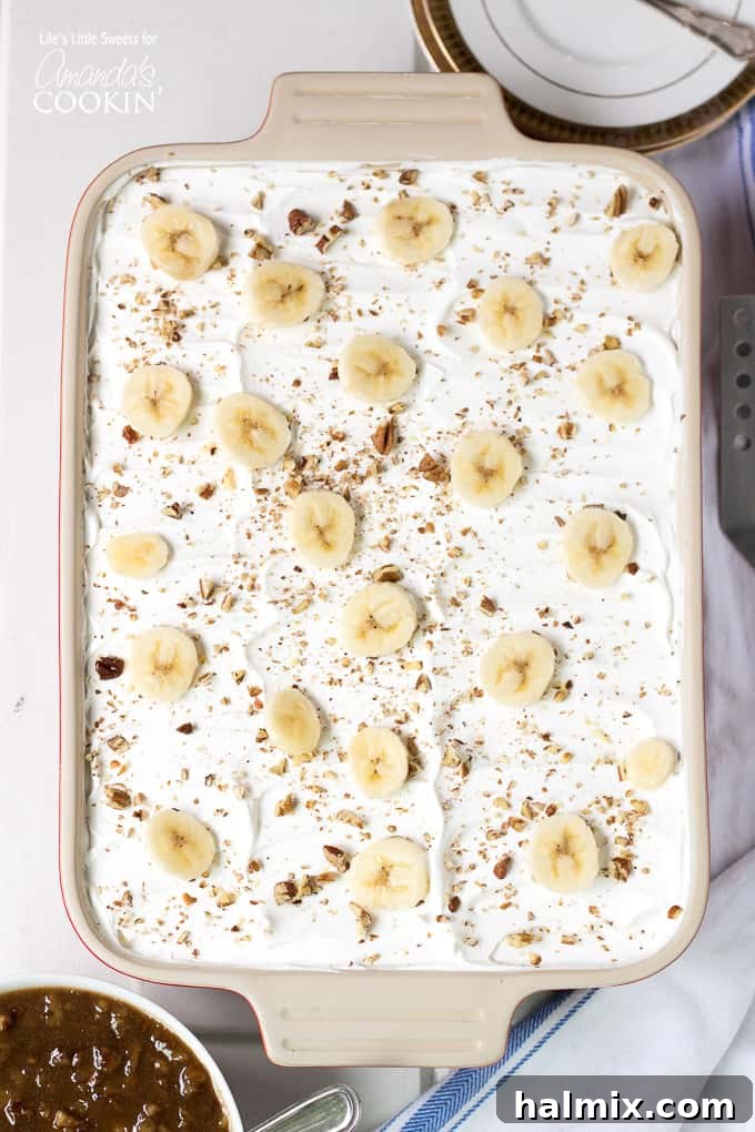 Layered banana dessert in a baking pan, topped with sliced bananas and pecans.