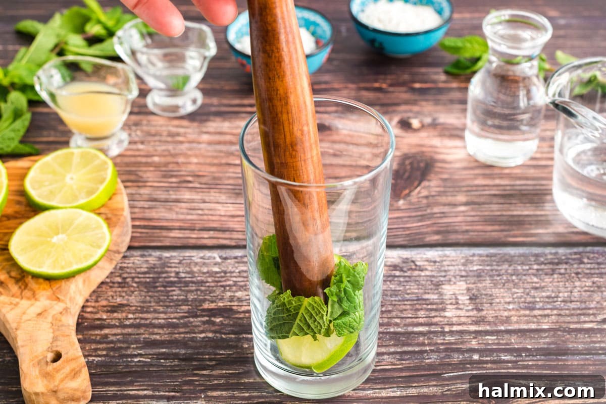 Gently muddling fresh mint leaves and a lime slice in a glass to release their aromatic flavors.
