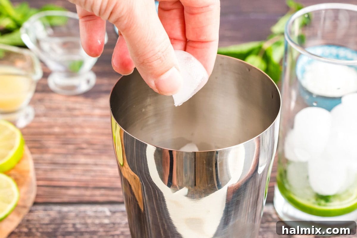 Adding ice to a cocktail shaker, preparing to mix the rum and coconut cream.