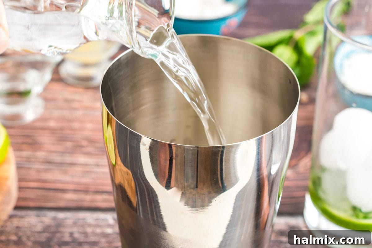 Pouring coconut rum into a cocktail shaker filled with ice, a key step for a tropical mojito.
