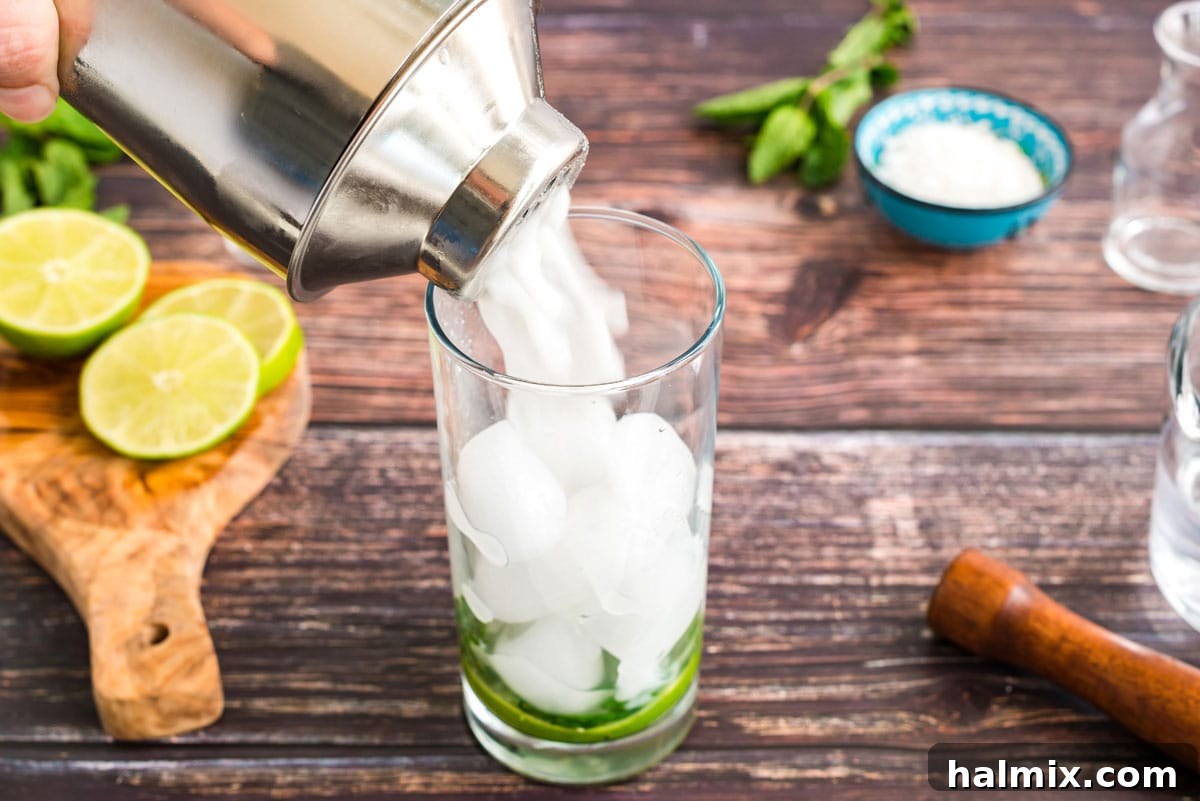 Straining the perfectly shaken coconut mojito mixture into a tall glass over muddled mint and ice.