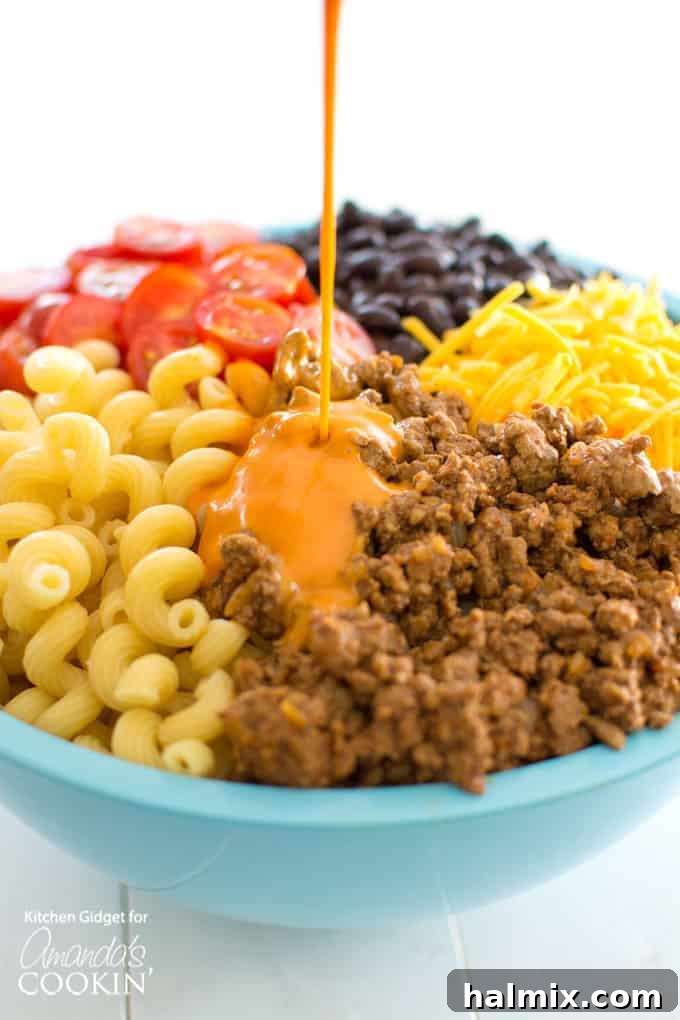 Watch as creamy French dressing is poured over a vibrant mix of taco pasta salad ingredients, ensuring every bite is bursting with flavor. A perfect addition for any summer salad! French dressing being poured over pasta salad ingredients