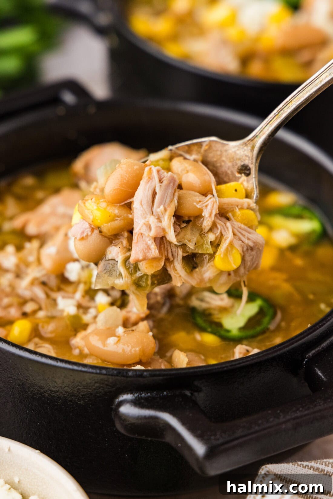 Spoon lifting up Crockpot White Chicken Chili from a bowl, showing shredded chicken and beans