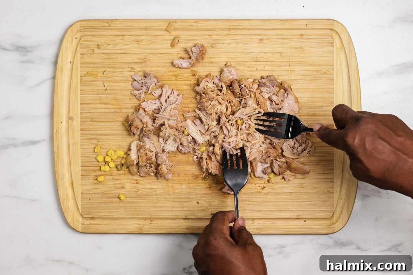 Shredding chicken with two forks on a cutting board, ready to be returned to the chili