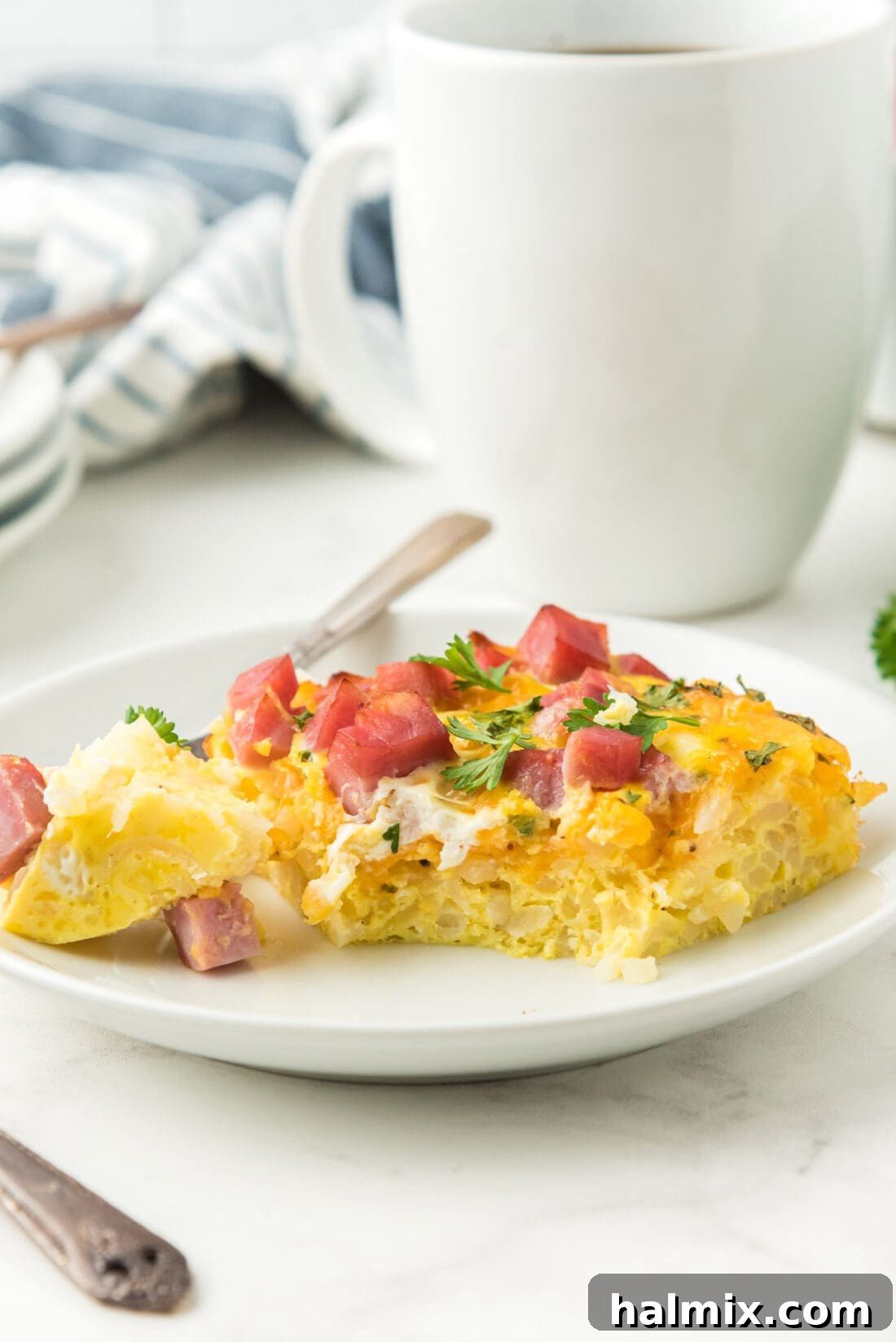A generous serving of breakfast casserole with ham and cheese on a white plate, ready to be enjoyed.