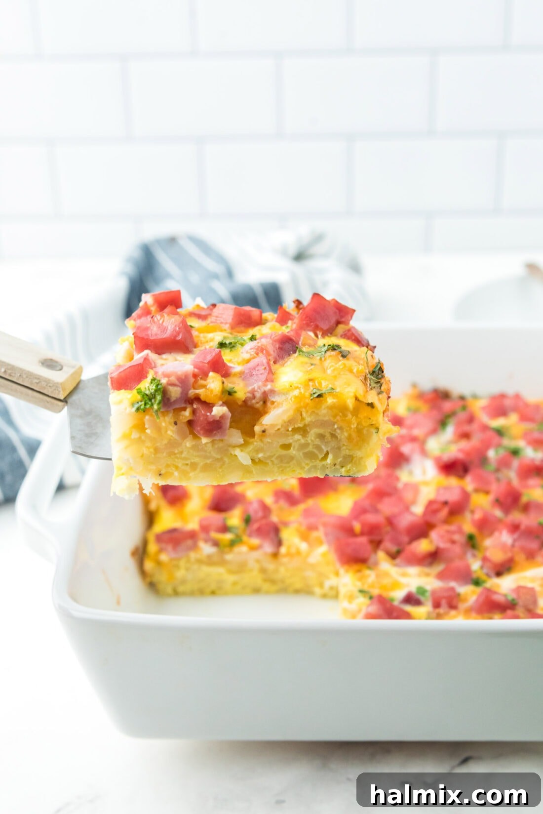 A spatula lifting a perfect serving of golden-brown breakfast casserole, showcasing the layers of ham, cheese, and hash browns.