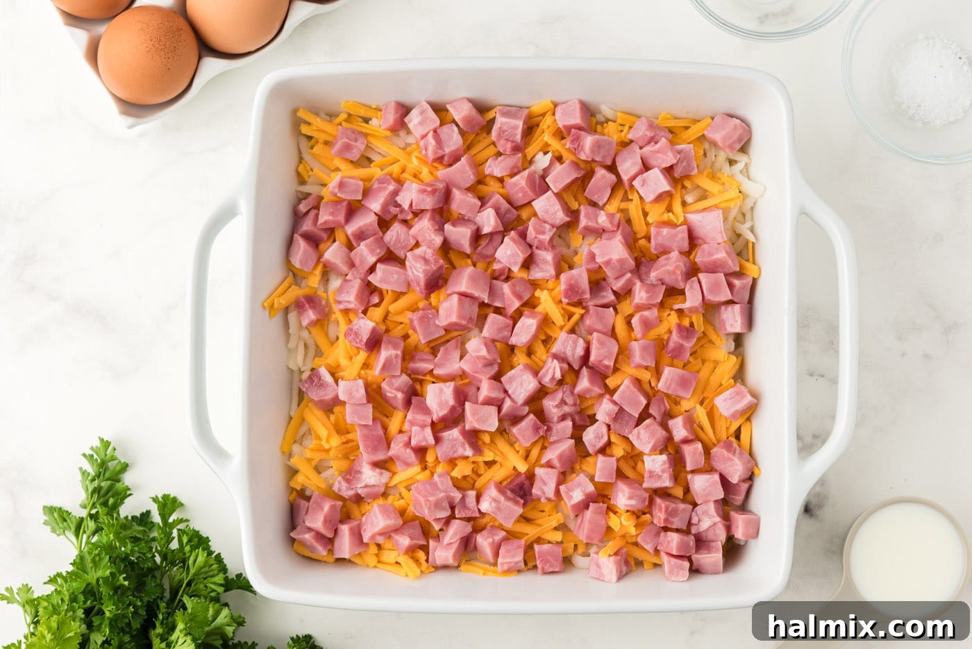 Diced ham cubes scattered over the cheese layer, completing the first set of savory layers.