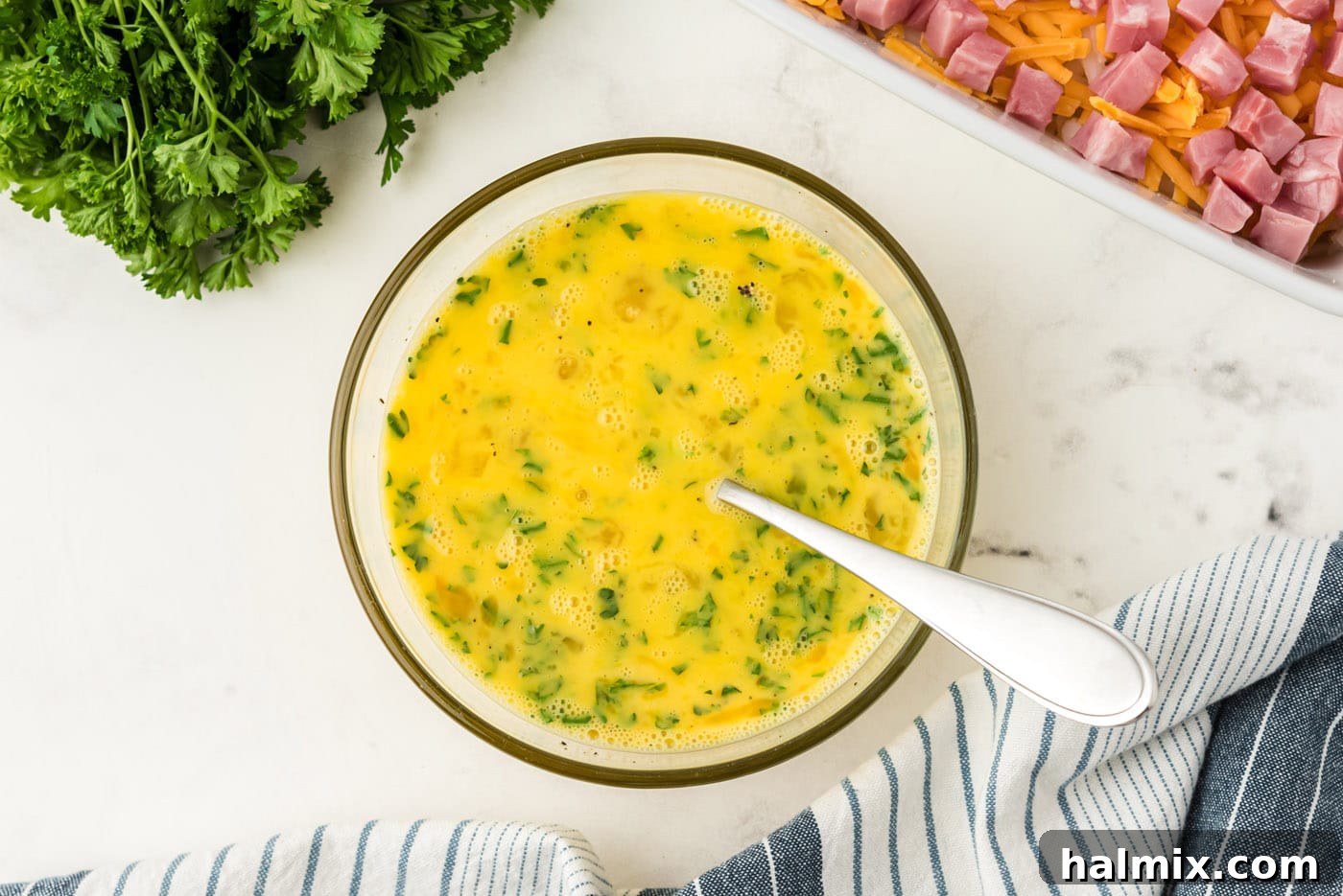 Eggs, milk, seasonings, and fresh parsley thoroughly mixed in a bowl, creating the liquid base for the casserole.