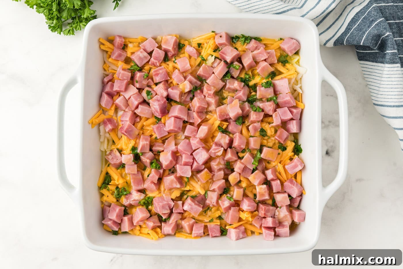 The egg mixture poured over the prepared layers of ham, cheese, and potatoes in the baking dish, ready for baking.