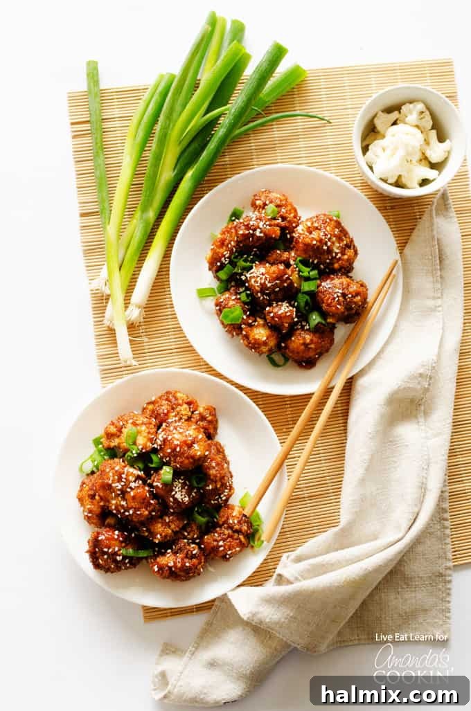 Two servings of sticky garlic cauliflower garnished with green onions and sesame seeds, presented in stylish white bowls.