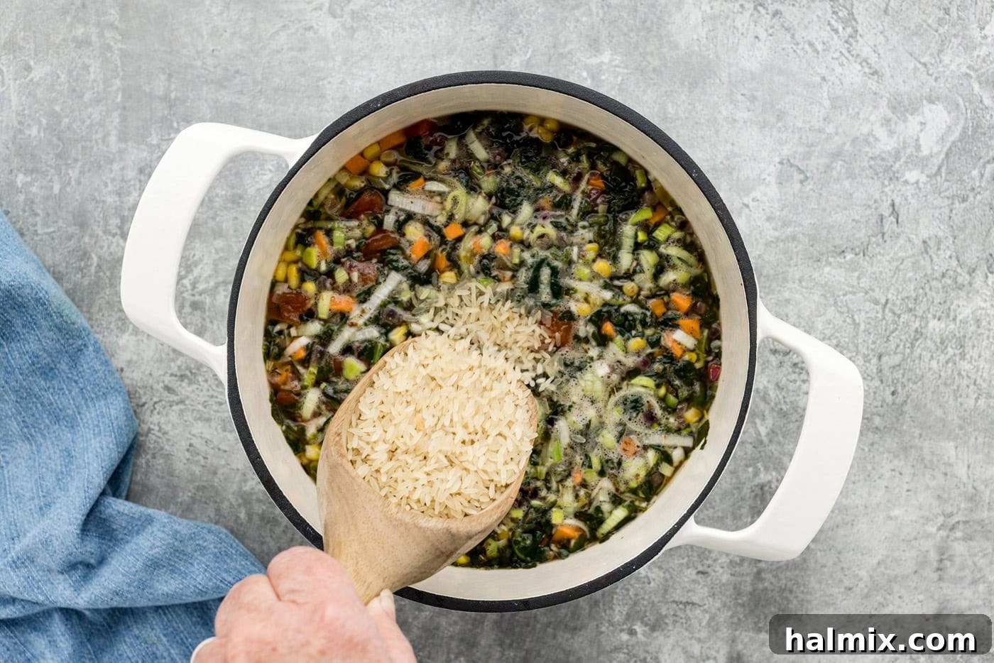 adding uncooked rice to vegetable soup in a pot, about to simmer