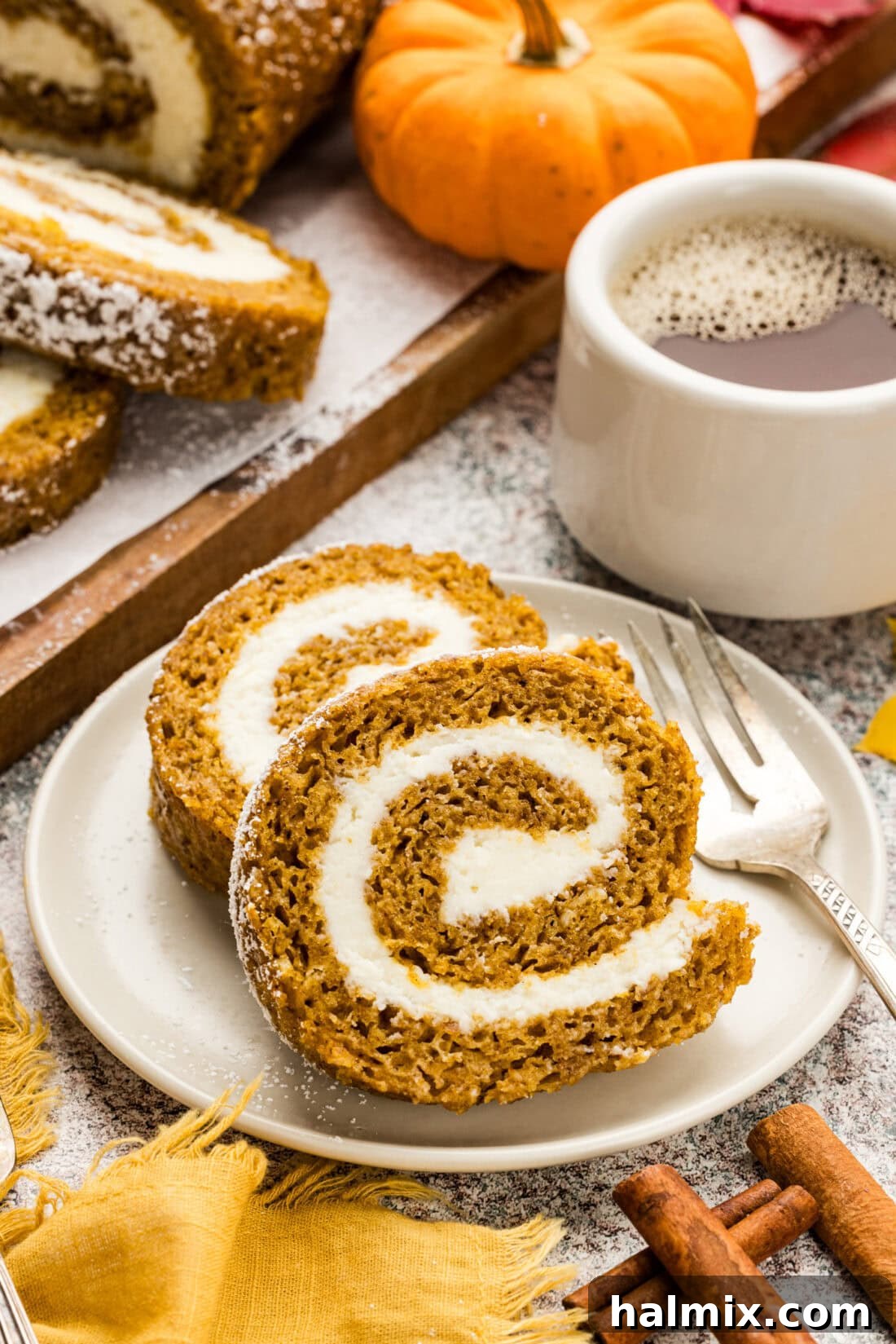 Two slices of Pumpkin Cake Roll on a plate, showcasing a perfect swirl of cake and frosting and dusted with confectioner's sugar.