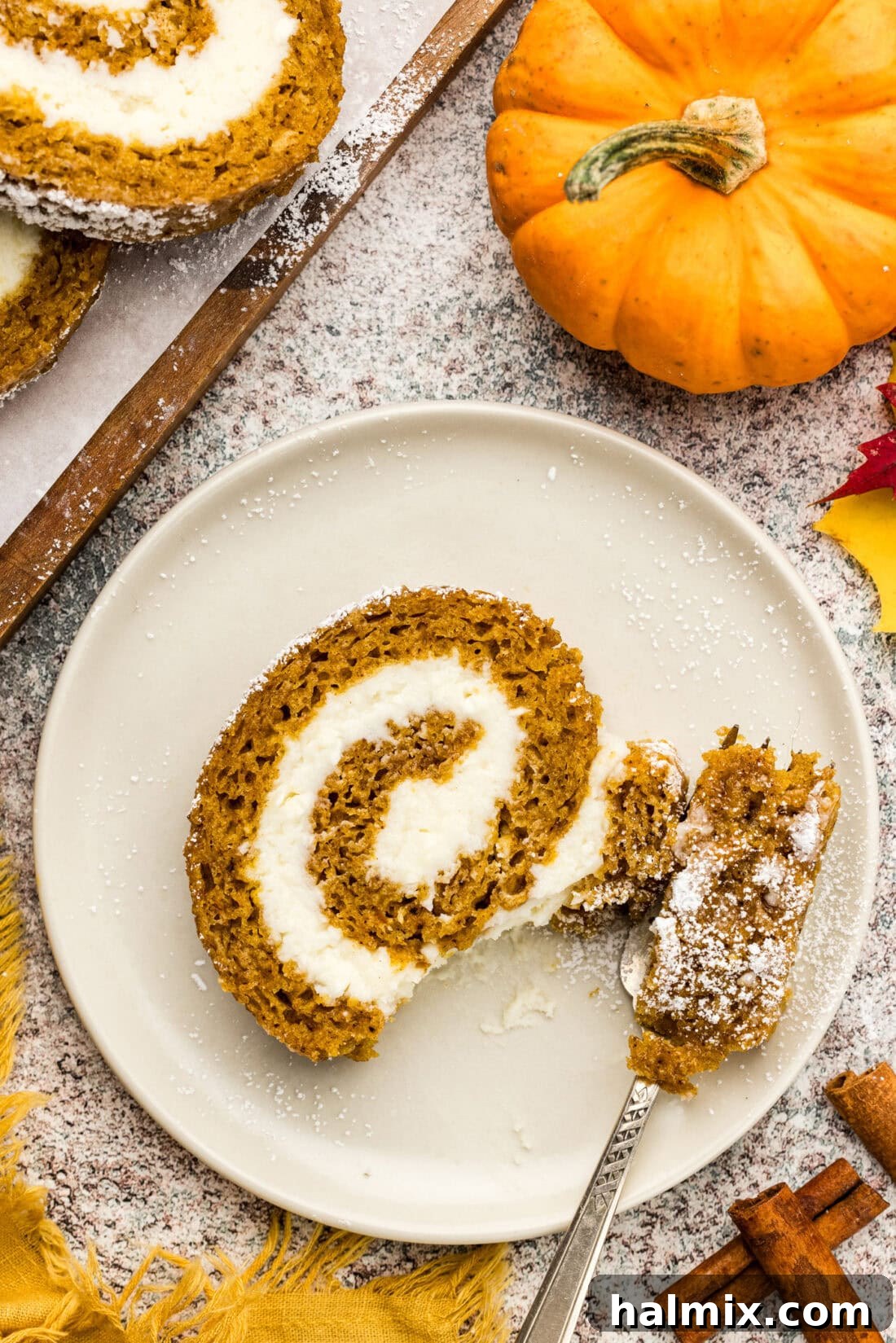 A single slice of Pumpkin Cake Roll on a white plate, with a bite taken out, clearly showing its moist texture and perfect cream cheese swirl.