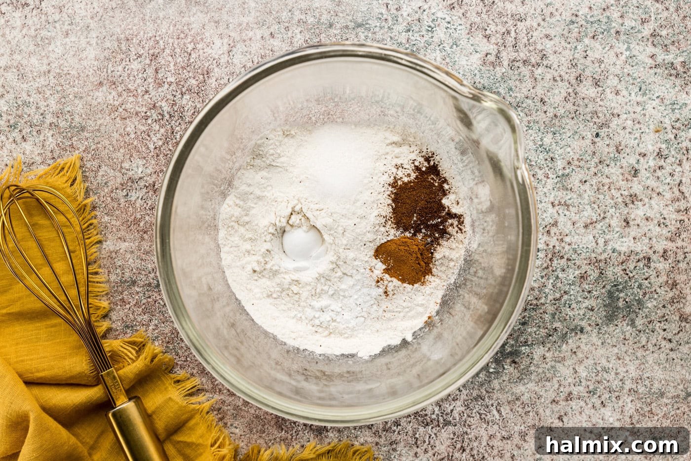 Flour and various spices combined in a mixing bowl, awaiting incorporation into the pumpkin cake batter.
