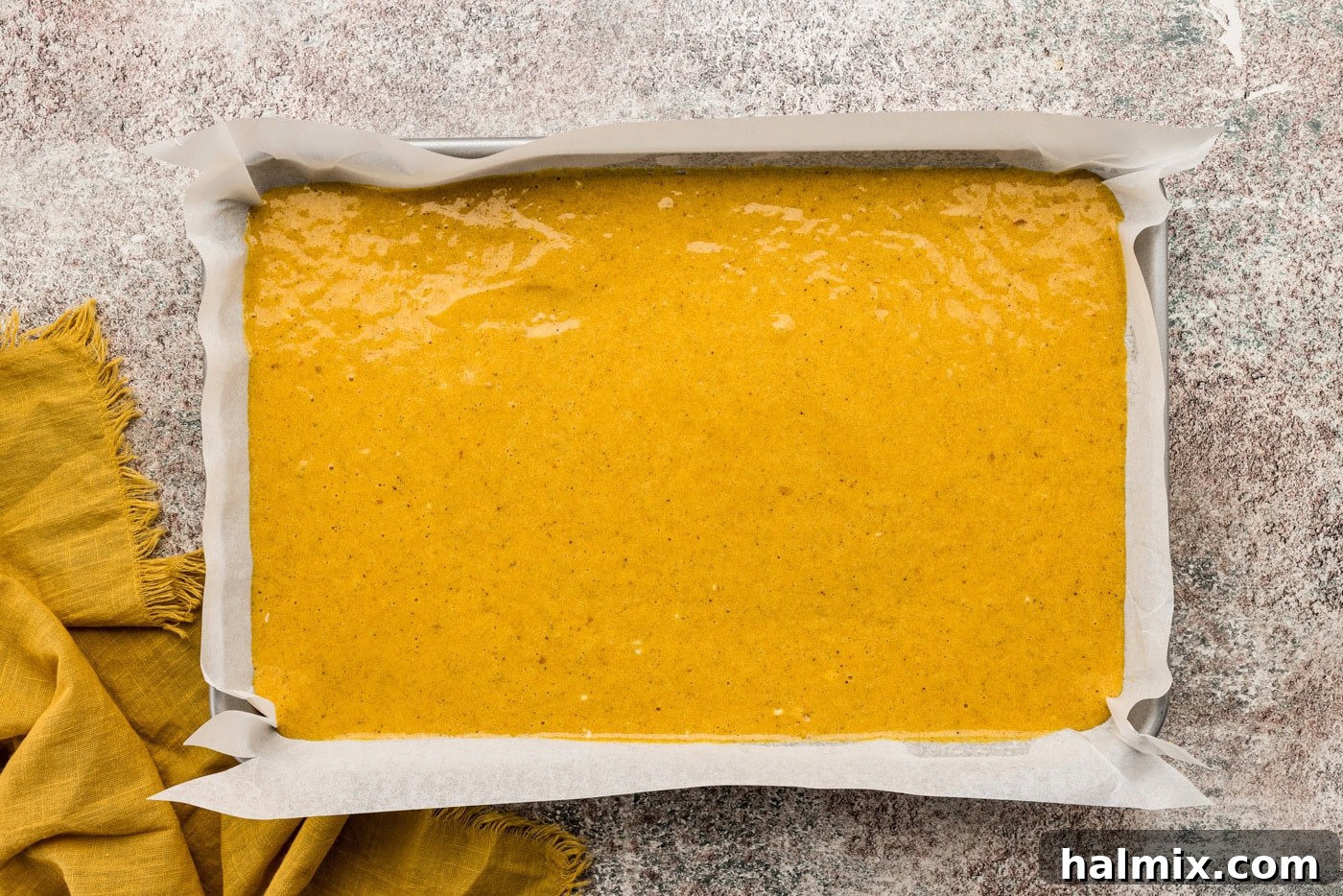 Smooth, spiced pumpkin cake batter spread perfectly into a parchment-lined jelly roll pan, ready for baking.