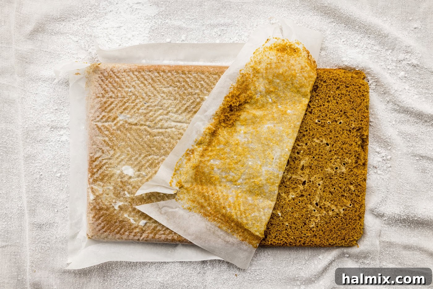 Carefully removing the parchment paper from the bottom of the freshly baked and slightly cooled pumpkin cake, preparing it for rolling.