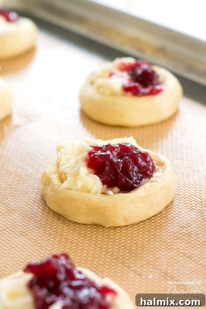 Crescent dough rounds filled with creamy vanilla cream cheese and vibrant whole berry cranberry sauce, ready for baking.