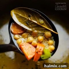 A ladle serving chickpea vegetable soup, emphasizing the hearty ingredients.