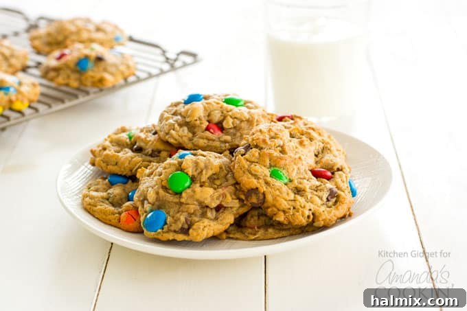 Monster Cookies: Irresistible peanut butter and oatmeal cookies packed with chocolate chips and colorful M&M's – a fun and easy recipe for everyone! #monstercookies #m&ms #cookierecipes #bestdessertrecipes #chocolate #peanutbutter #peanutbuttercookies #oatmeal #oatmealcookies Monster cookies on a plate with a glass of milk, a perfect pairing for this delicious treat.