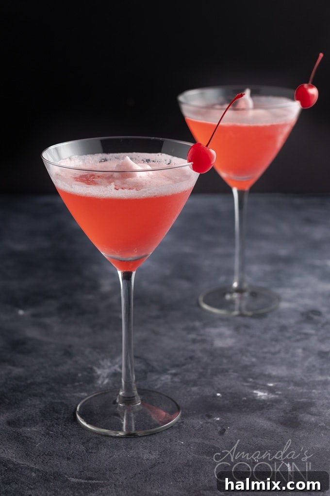 Two exquisite Pink Lady Cocktails in martini glasses, showcasing their frothy texture and inviting pink hue, perfect for a celebratory toast. two pink ladies - martini glasses