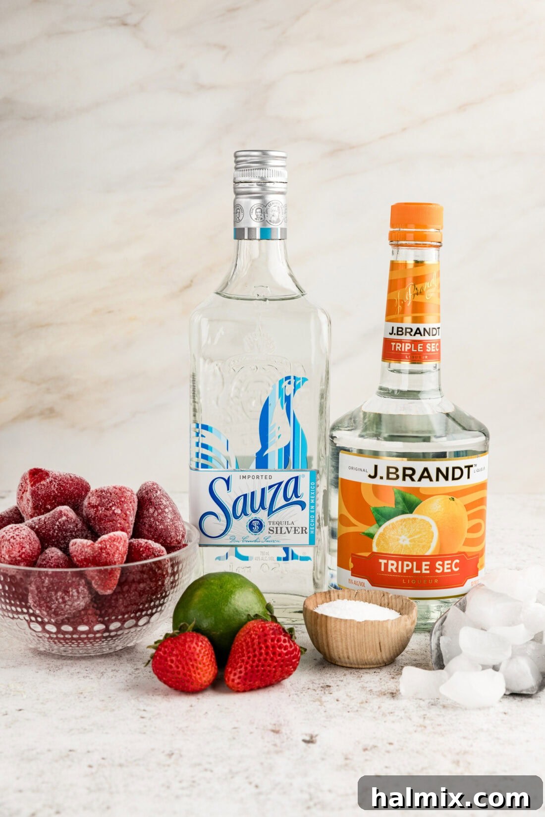 Ingredients for Frozen Strawberry Margarita laid out, including frozen strawberries, tequila, triple sec, lime, and ice