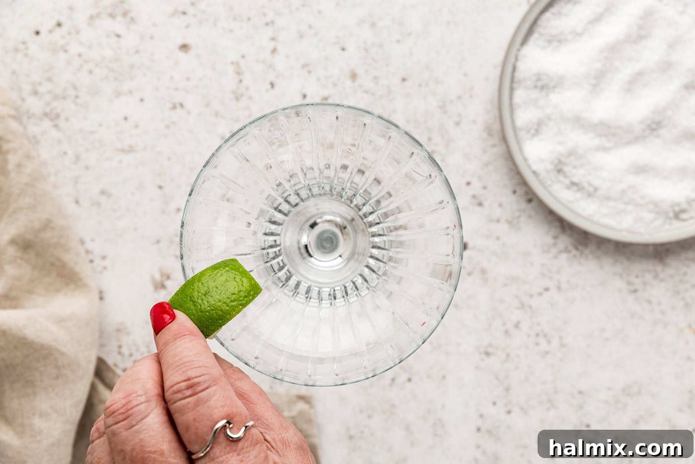 Hand rubbing a lime wedge over the rim of a margarita glass to moisten it for salt