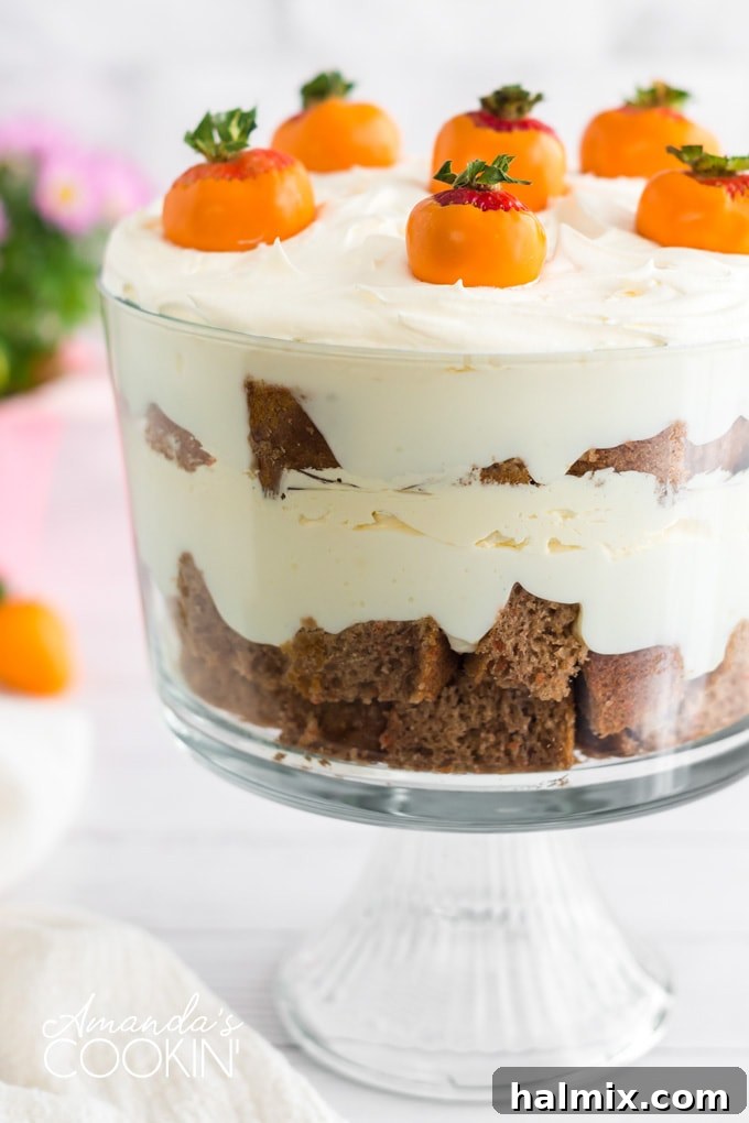 Layers of moist carrot cake, creamy cheesecake filling, and whipped topping in a glass trifle bowl, garnished with orange-dipped chocolate strawberry carrots.