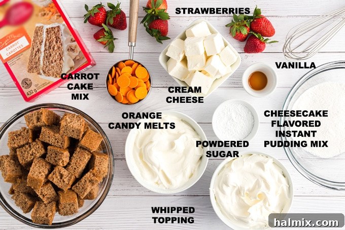 All the ingredients for a carrot cake trifle laid out on a white surface, including cake mix, pudding mixes, cream cheese, sugar, vanilla, whipped topping, orange candy melts, and strawberries.