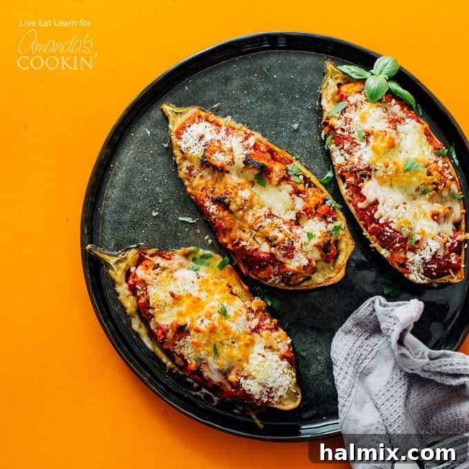Two halves of stuffed baked eggplant parmesan on a black plate, showing the rich filling and melted cheese
