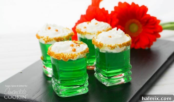 A tray of green jello shots with gold sugar rims and whipped cream, ready to serve, presented as an ideal treat for St. Patrick's Day festivities.