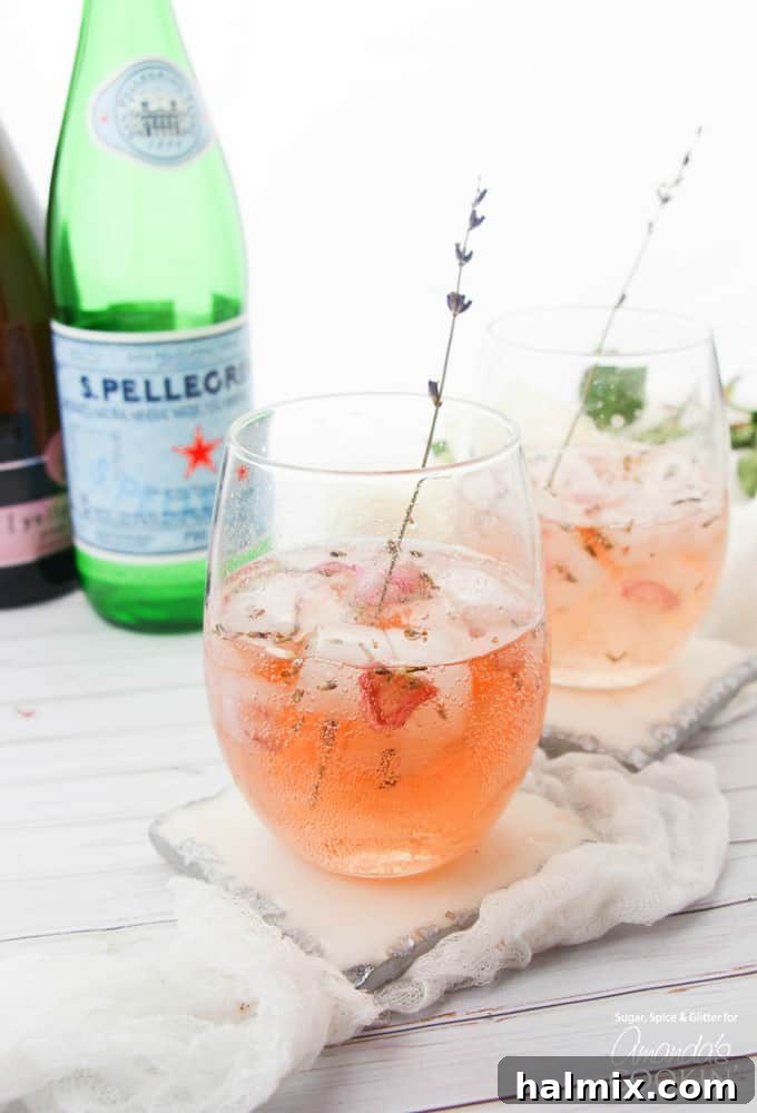 Elegant Lavender Rose Spritzer: made with fresh lavender, rose petals and sparkling rosé. Ideal for brunch, bridal showers, and summer entertaining! Lavender rose spritzer in wine glasses with lavender stem garnish, set in a bright, elegant scene