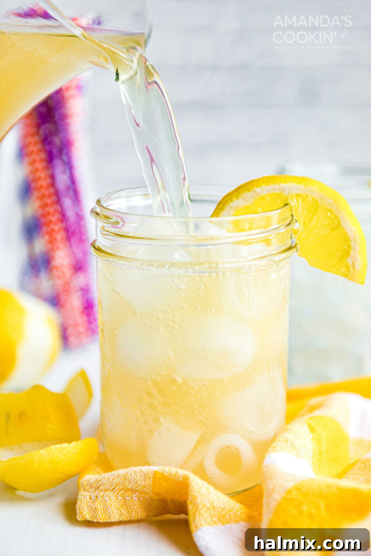 Lynchburg's Golden Refreshment 2 Pouring Lynchburg lemonade into a mason jar glass from a pitcher, garnished with lemon.