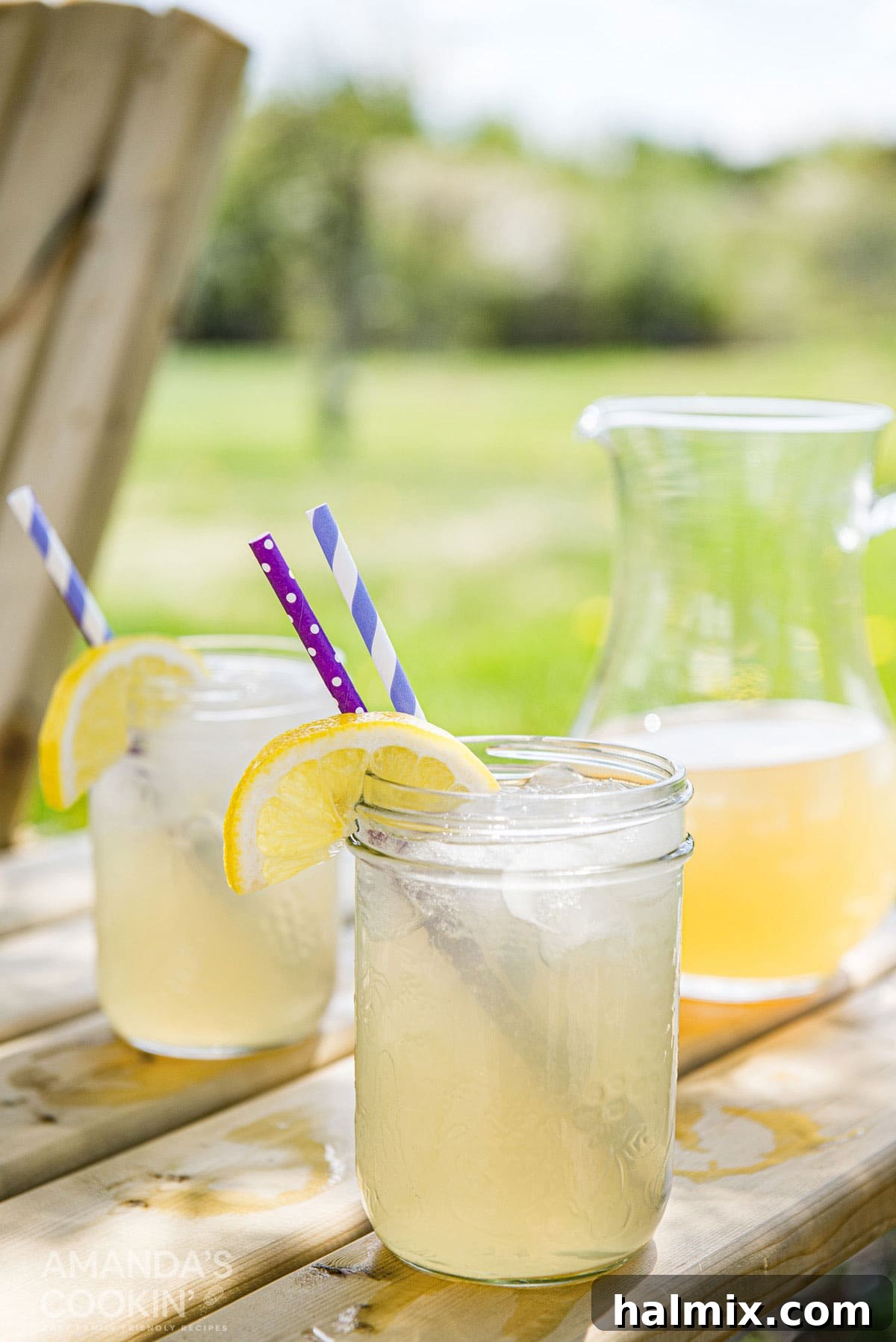 Lynchburg's Golden Refreshment 3 A pitcher of Lynchburg lemonade and two mason jars resting on a picnic table. Mason jars have a wedge of lemon and a straw in each glass, perfect for a summer BBQ.