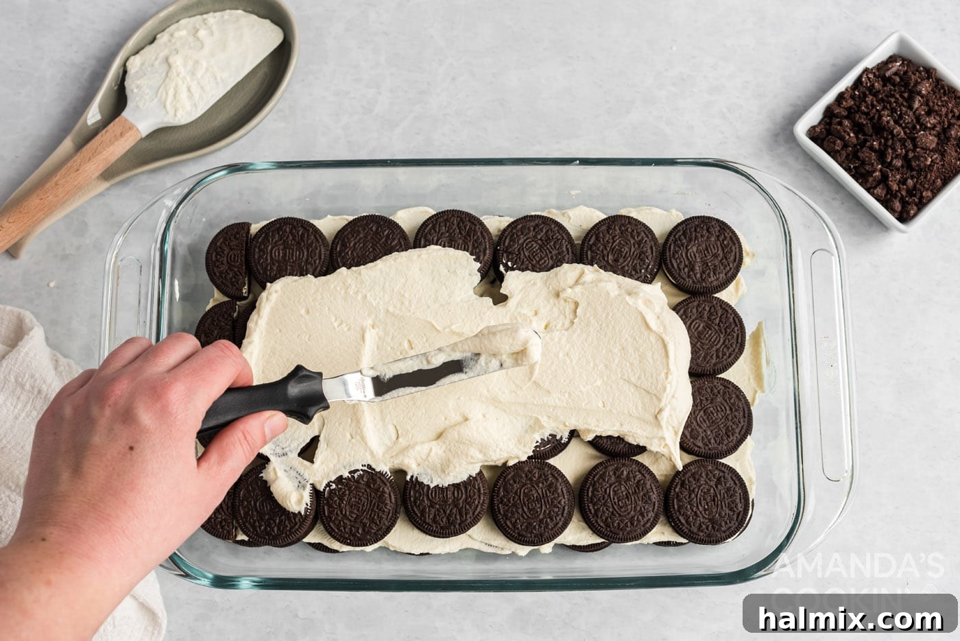 spreading whipped topping over the top of oreos in a baking dish