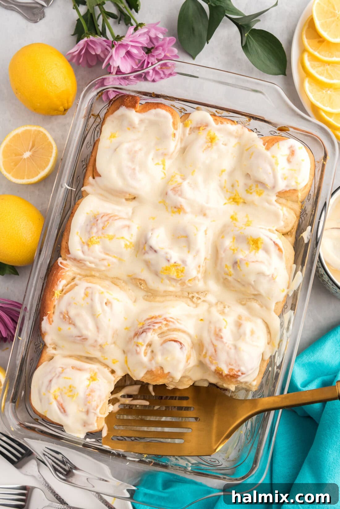 Pan of freshly baked Lemon Sweet Rolls with a spatula in it, glazed with lemon cream cheese icing.