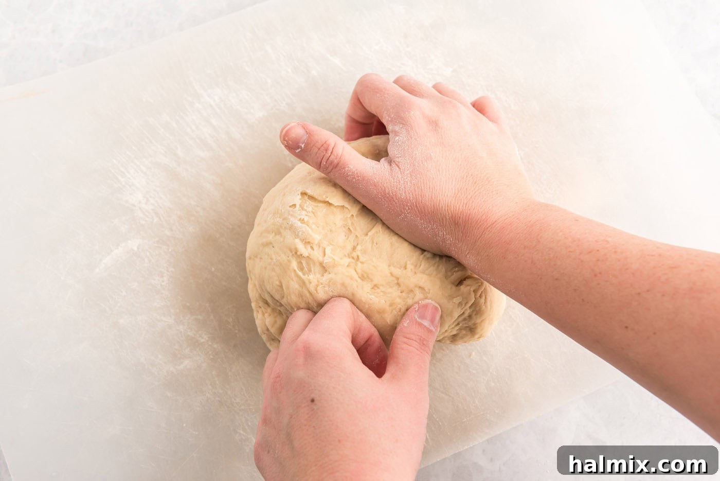 Hands kneading a ball of dough on a floured surface.