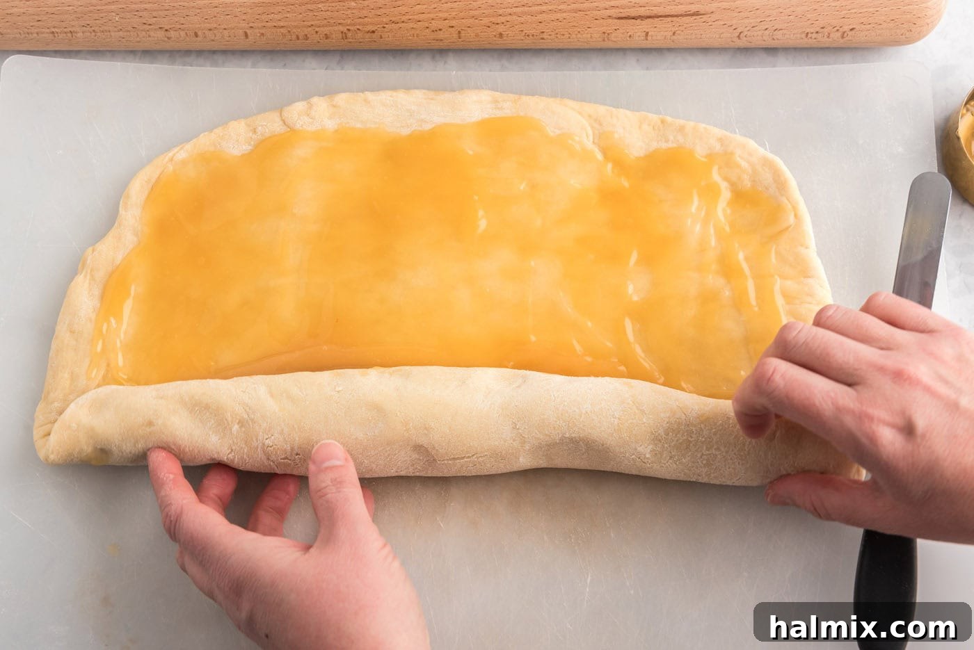 Rolling the lemon sweet roll dough into a tight log after spreading the curd.