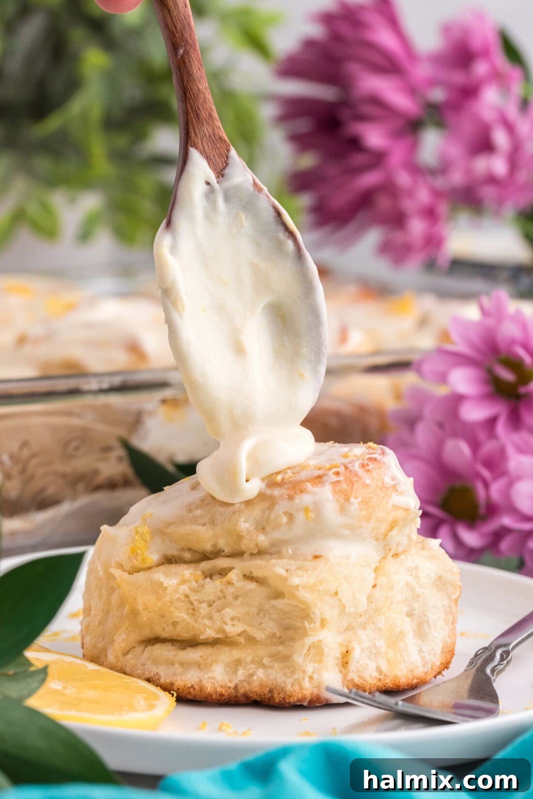 Lemon cream cheese frosting being drizzled generously onto a warm lemon sweet roll.
