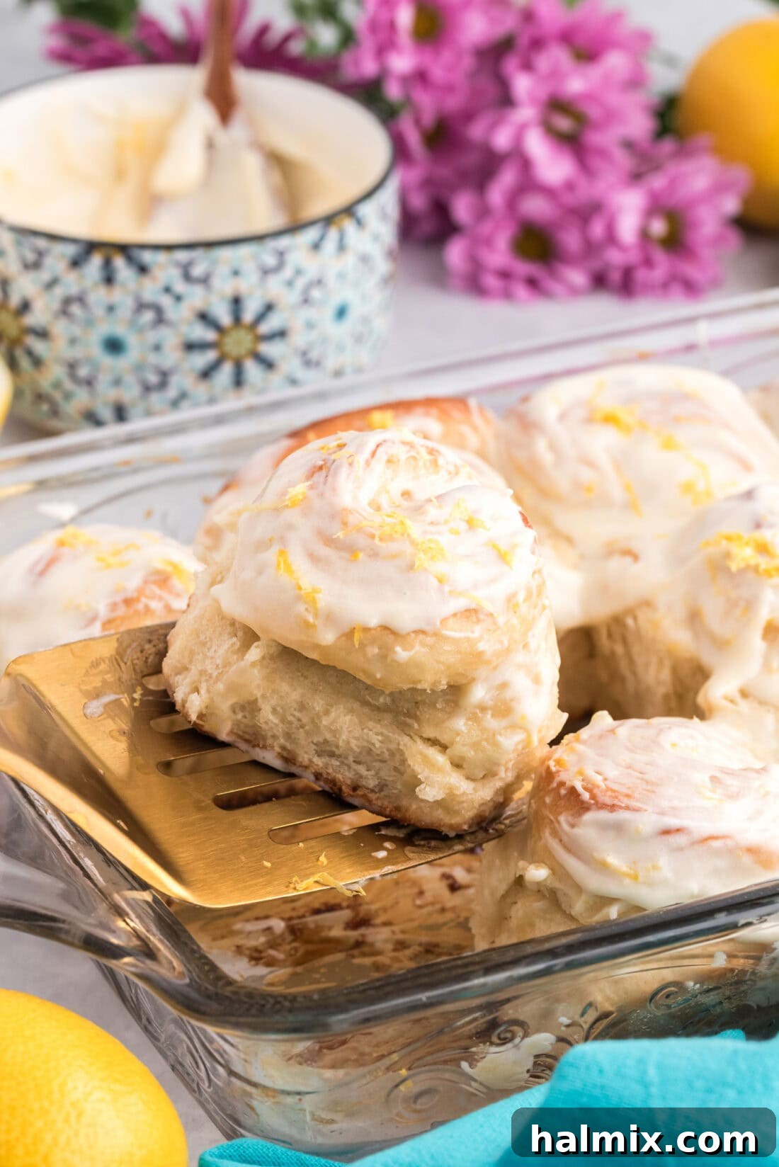 A single Lemon Sweet Roll being lifted from the baking pan, showcasing its fluffy texture and lemon curd swirl.