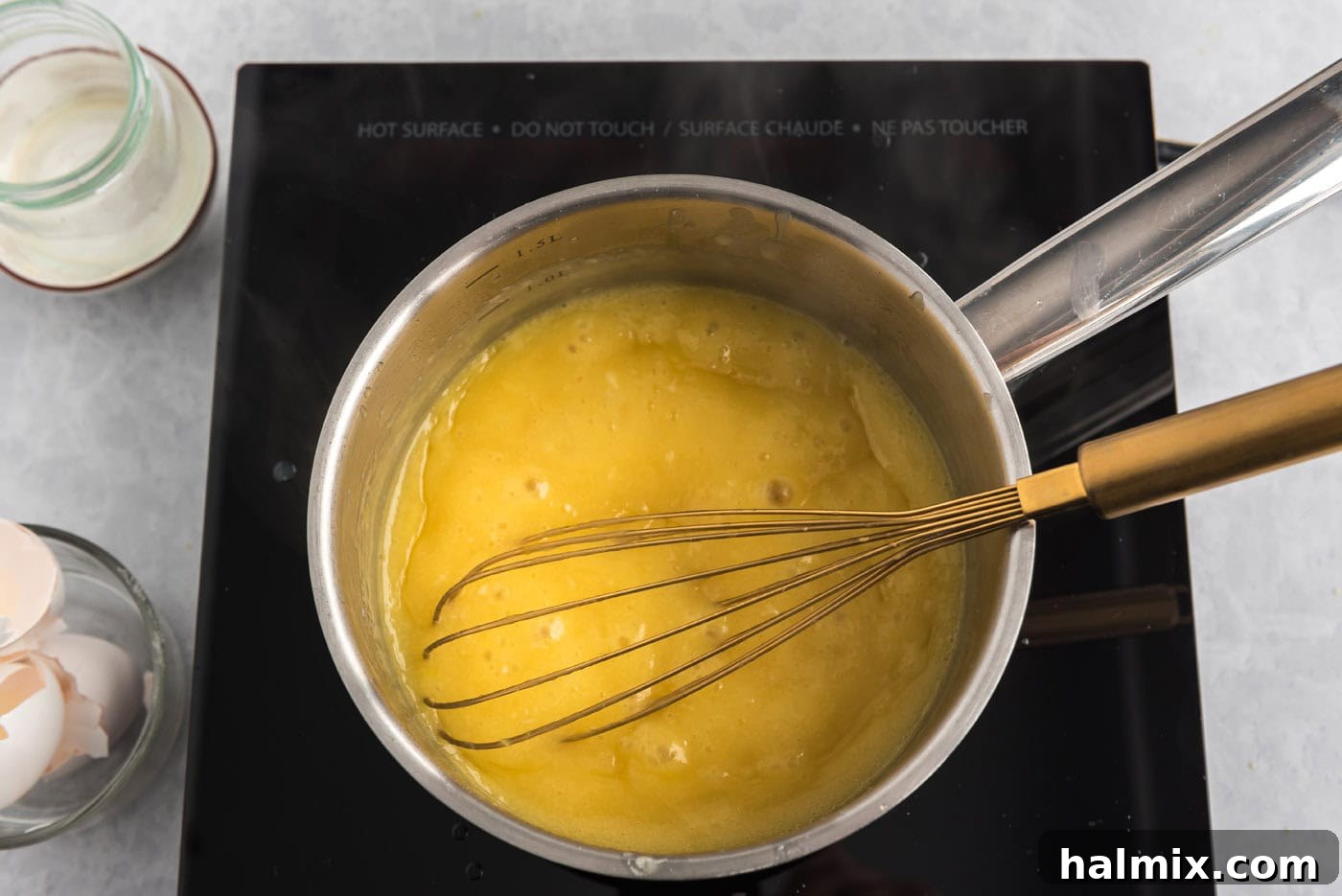 Homemade lemon curd in a saucepan with a whisk, showing its thick consistency.