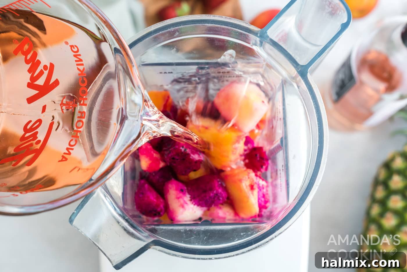Pouring a vibrant rosé wine into a blender filled with an assortment of colorful frozen fruits.